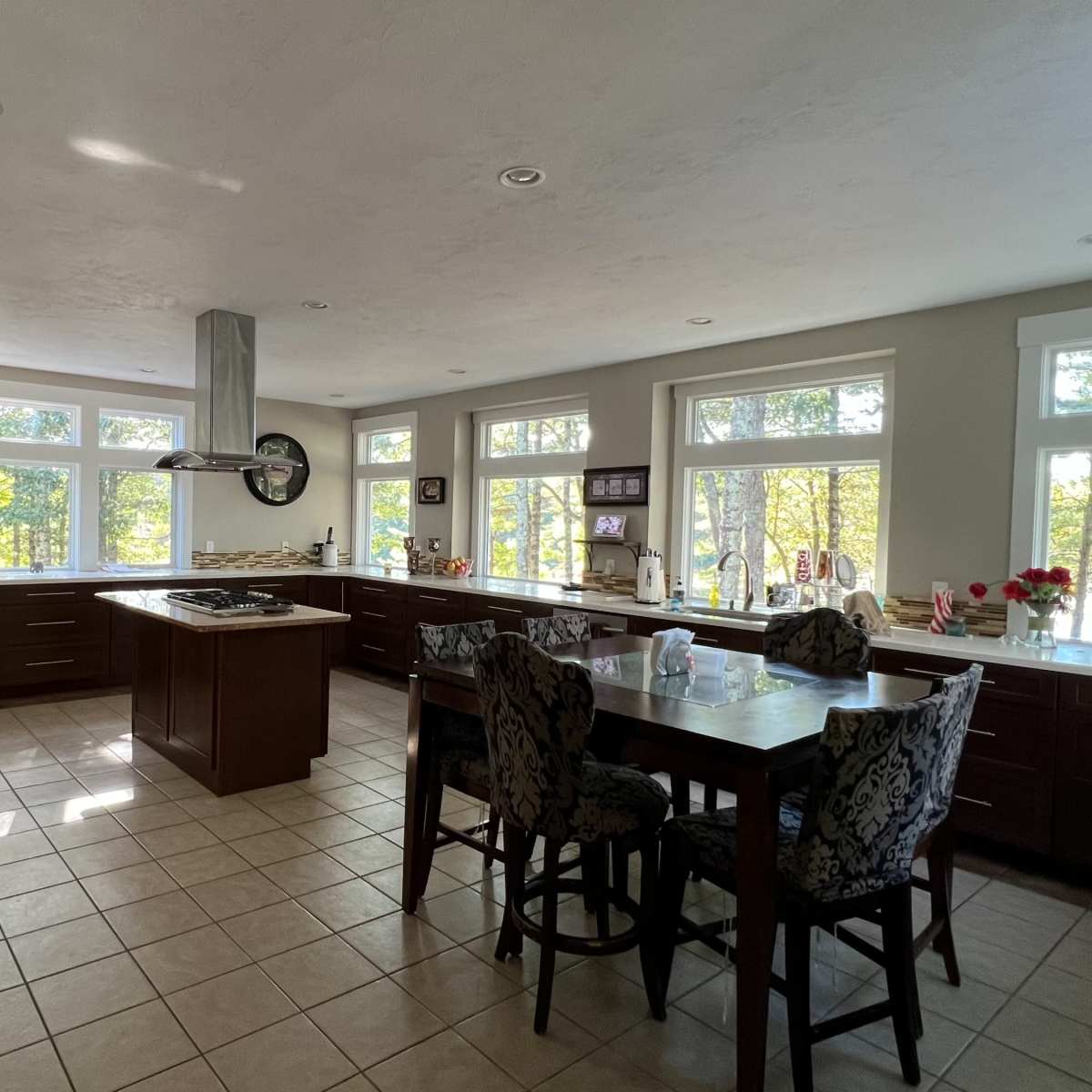 A spacious kitchen features large windows overlooking a natural landscape, with modern appliances and a central island.