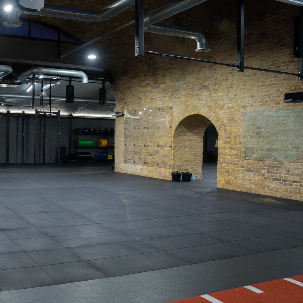 A spacious gym area with exposed brick walls, large windows, and various fitness equipment situated in the background.