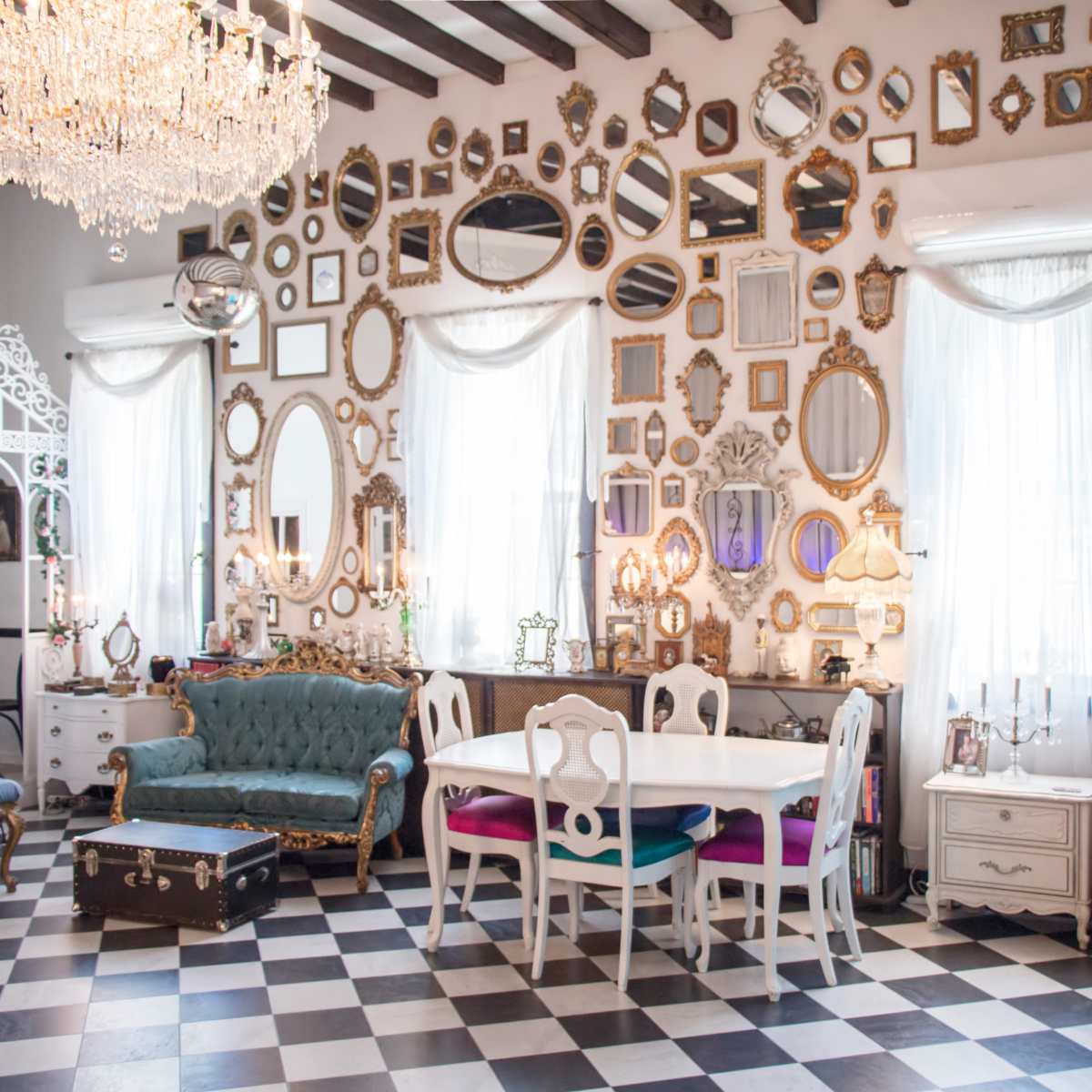 The room features a chic layout with a checkered floor, a dining table surrounded by colorful chairs, and walls adorned with numerous mirrors and frames.