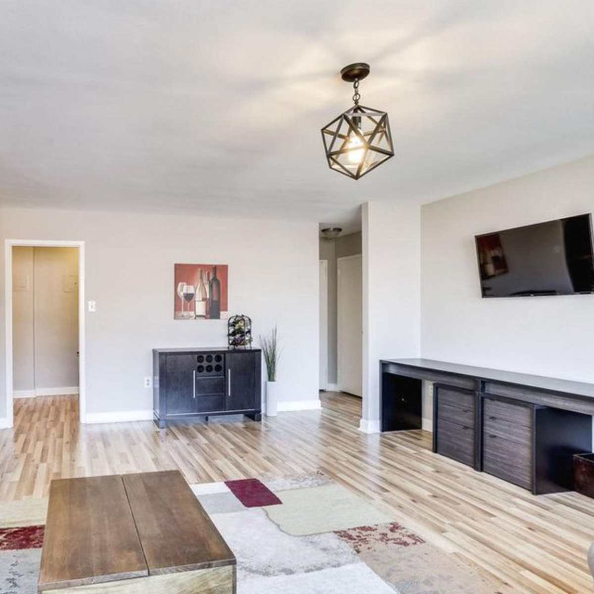 A modern living room featuring a gray sofa, a wooden coffee table, and a flat-screen TV mounted on the wall, with light wood flooring and minimal decorative elements.