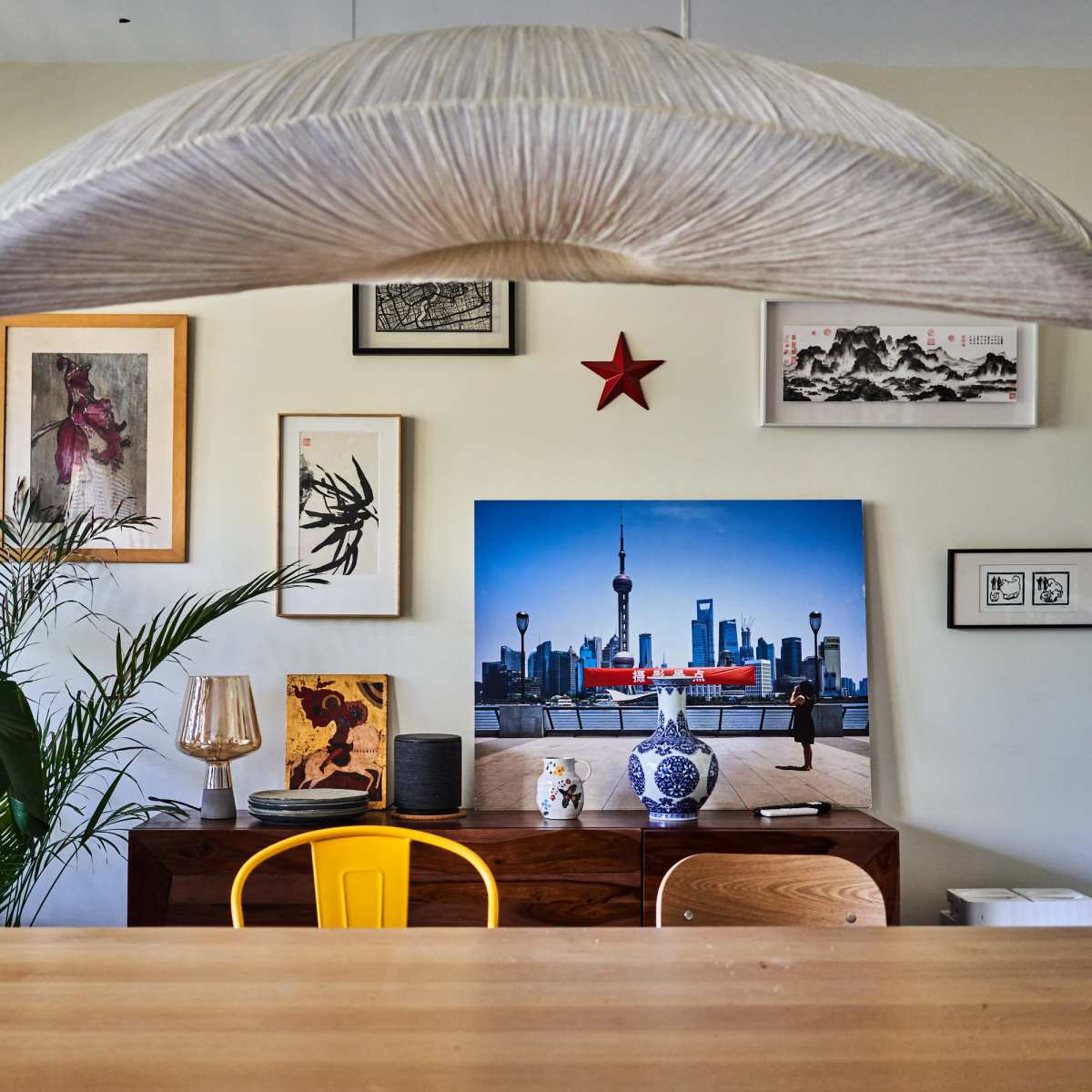 A modern dining area features a wooden table surrounded by chairs, with various framed art pieces and a large photograph of a city skyline on the wall.