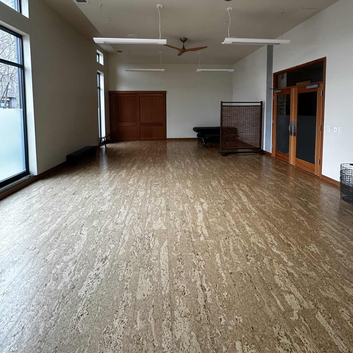 A spacious, empty room with large windows, wooden ceiling fans, and a wooden sliding door on one side.