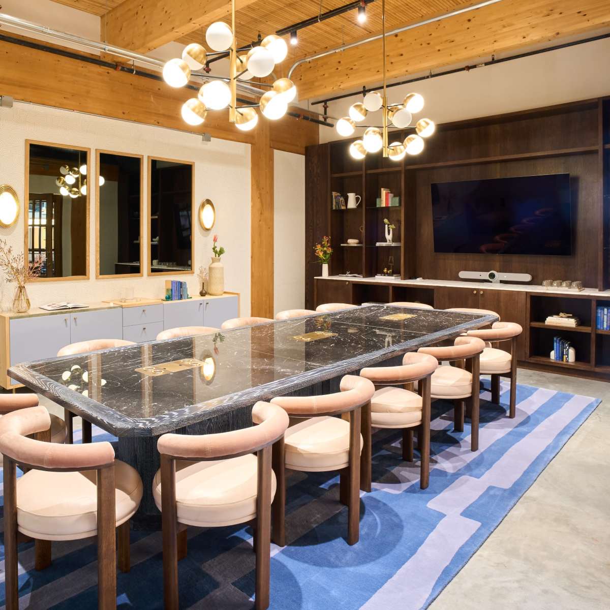 A spacious dining area features a large marble table surrounded by upholstered chairs, complemented by modern lighting and a wooden accent wall.