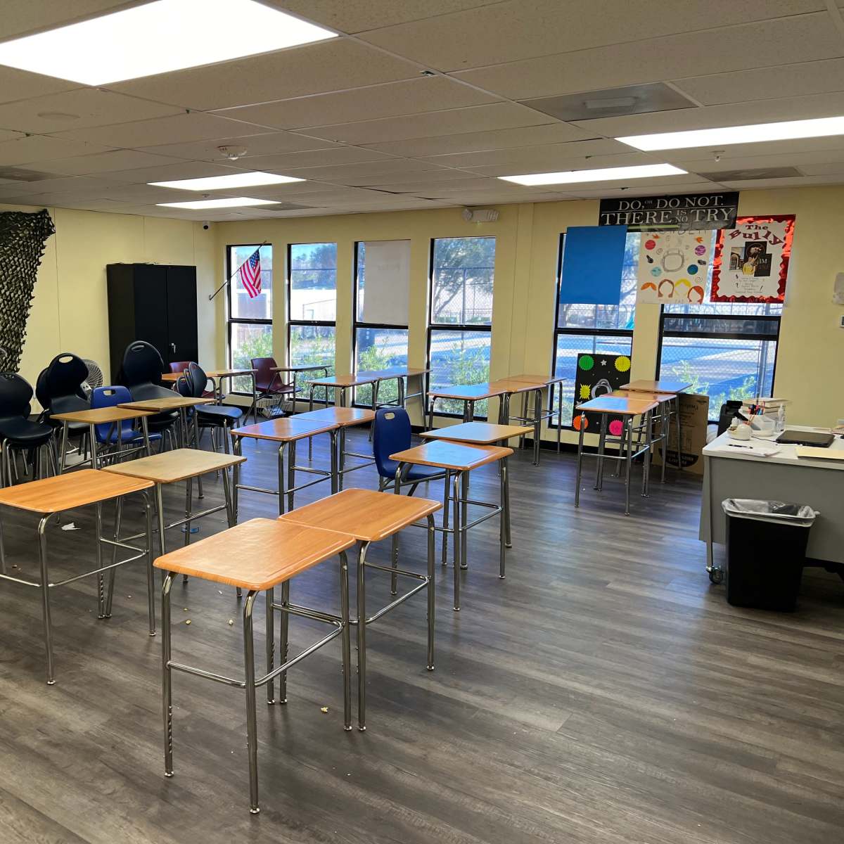 A classroom with several empty desks arranged in a semi-circular layout and large windows allowing natural light to enter.
