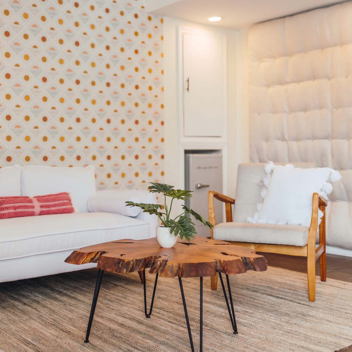 The scene features a modern living room with a white sofa, a wooden coffee table, and patterned wallpaper.