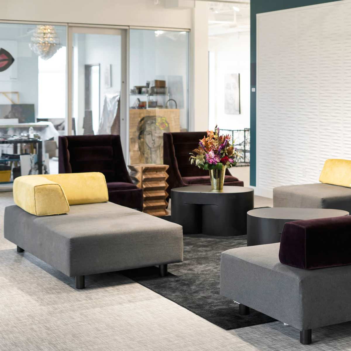 A modern lounge area with gray and black sofas, a round table, and a vase of flowers on a black carpet.