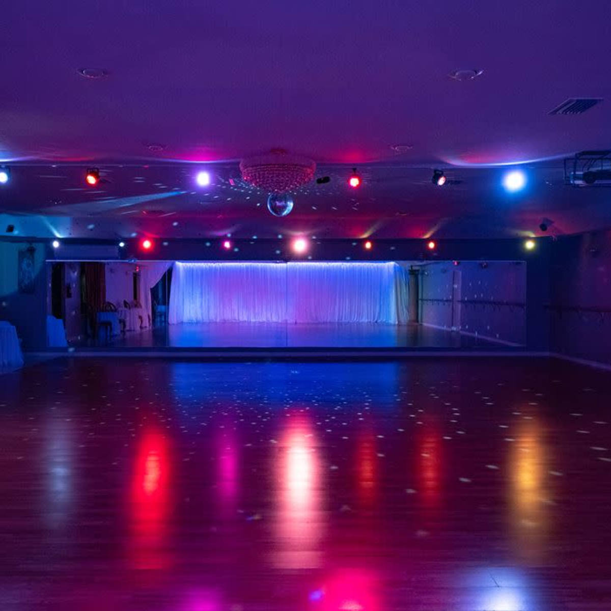 A brightly lit dance studio with colorful spotlights and reflective surfaces on the floor.
