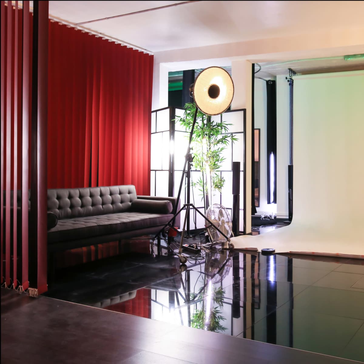 A photography studio with a black couch, a large light source on a stand, and a green backdrop.