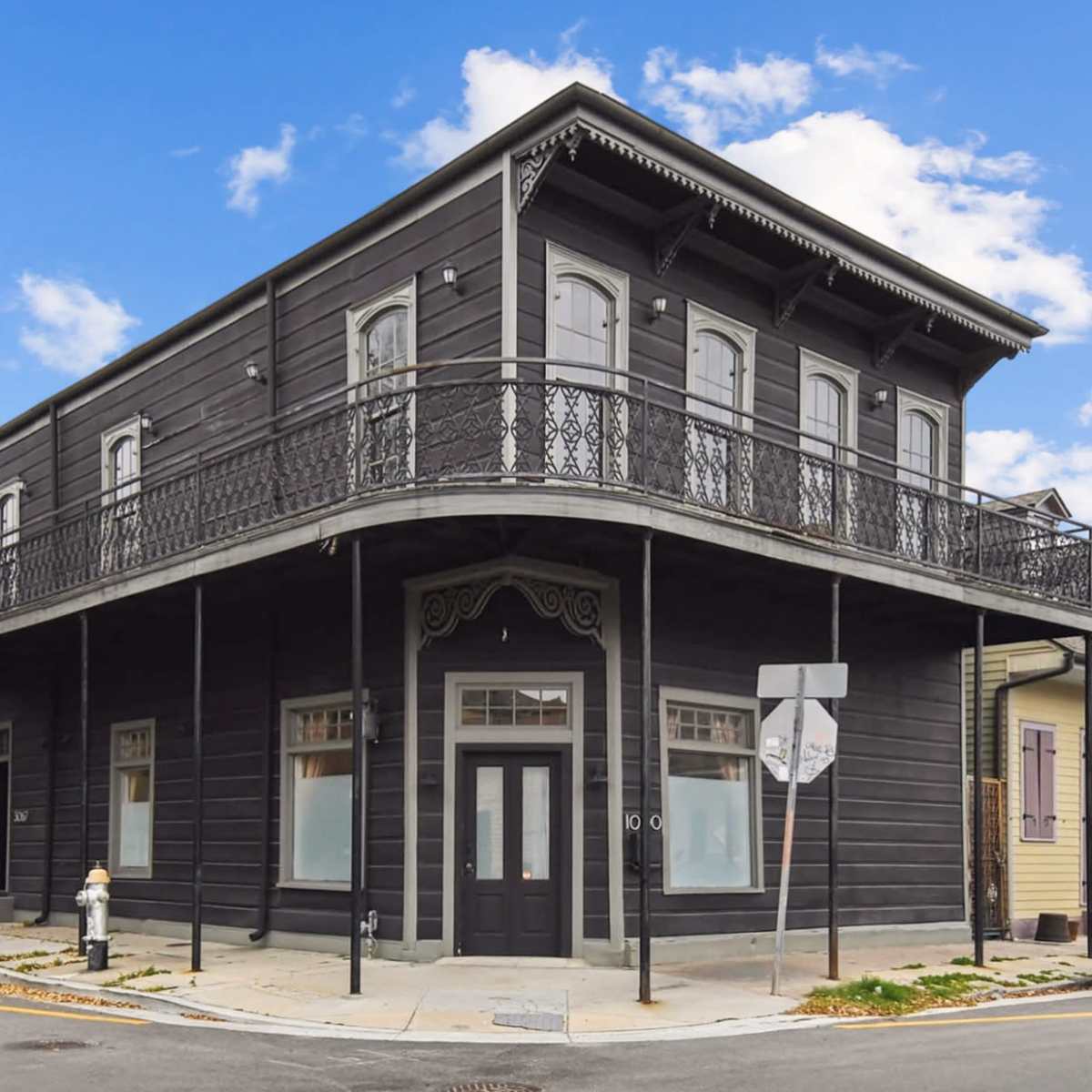 A two-story, dark-colored building with a decorative balcony and large windows located at a street corner.