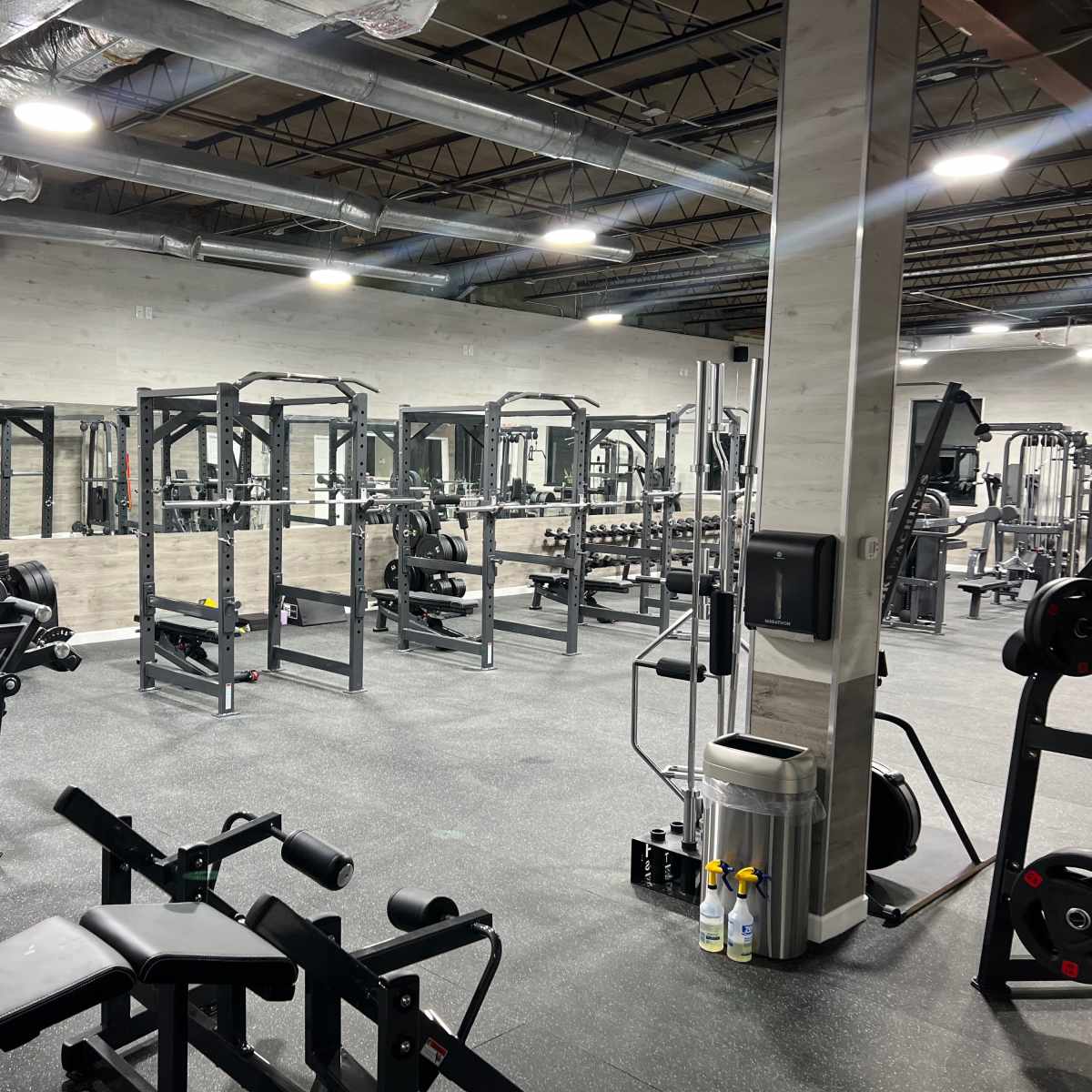 A spacious gym with various workout equipment, including weight machines and squat racks, arranged neatly on a rubberized floor.