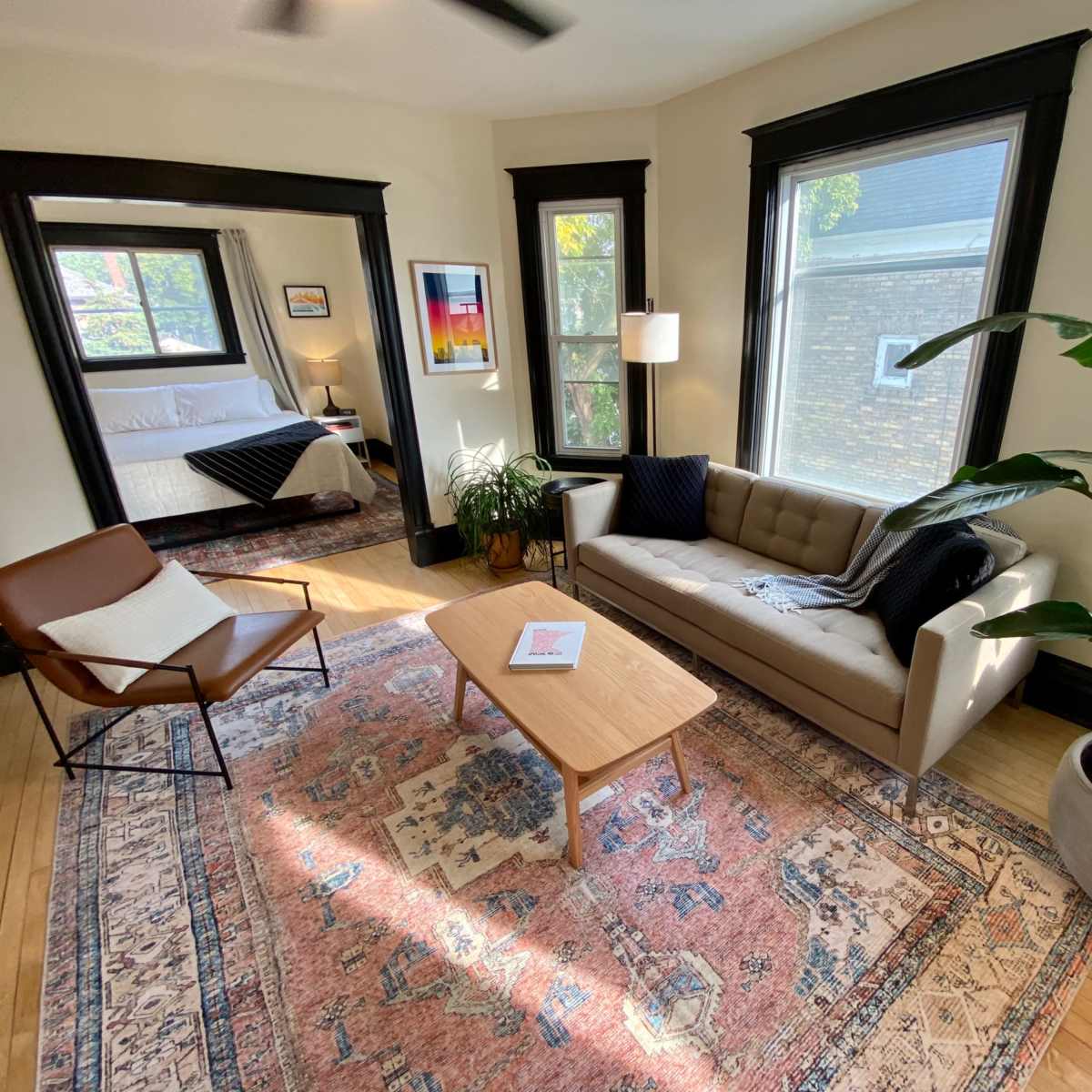 A living room with a sofa, a coffee table, a chair, a potted plant, and large windows that provide natural light.