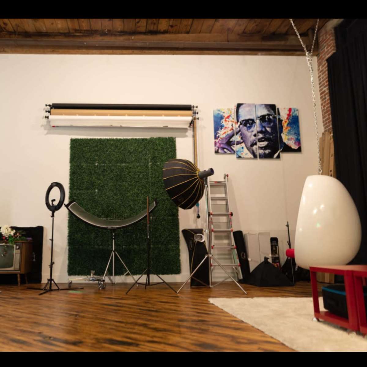 A photography studio with a green wall, various lighting equipment, props, and a ladder.