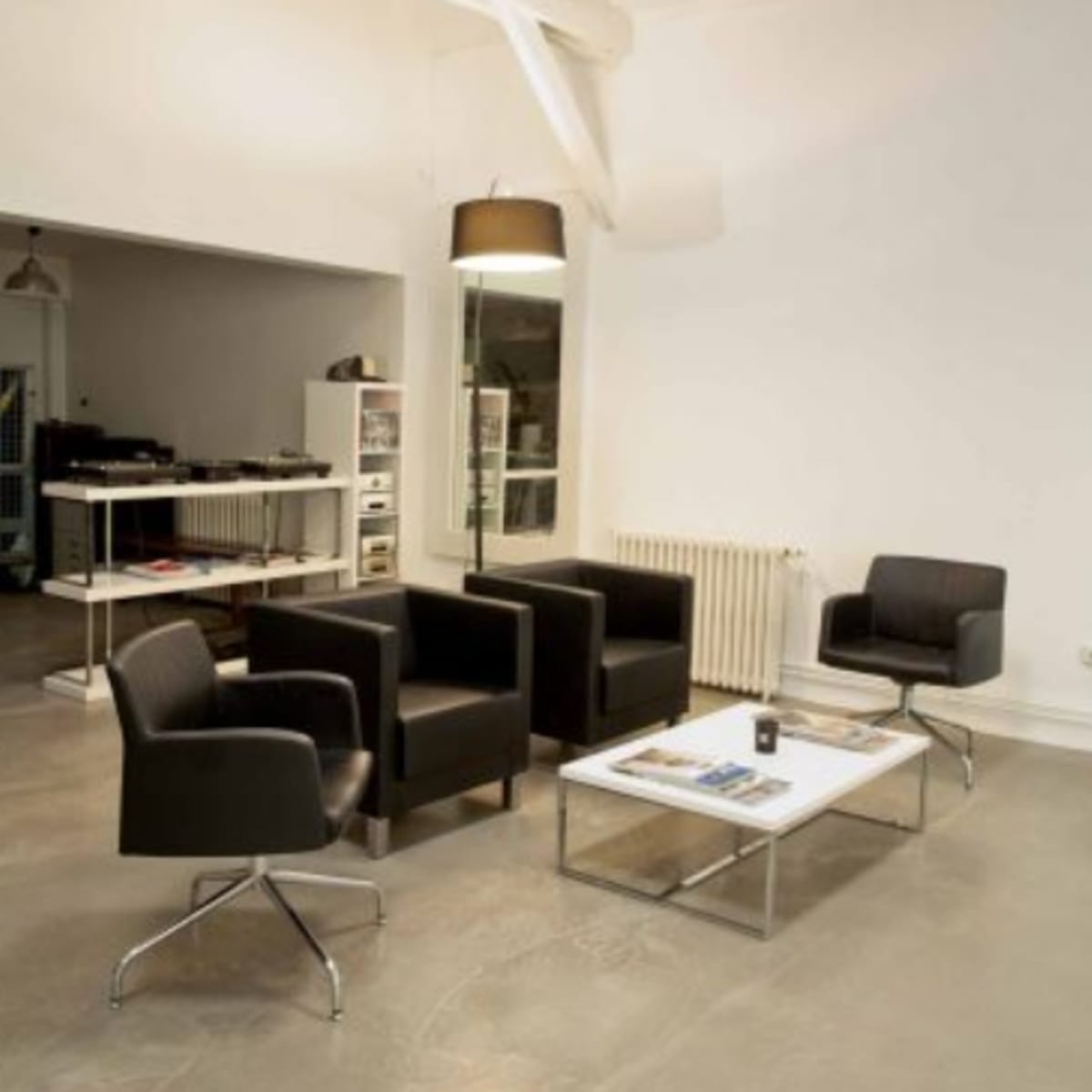 A modern interior space features four black armchairs arranged around a glass coffee table on a polished concrete floor.