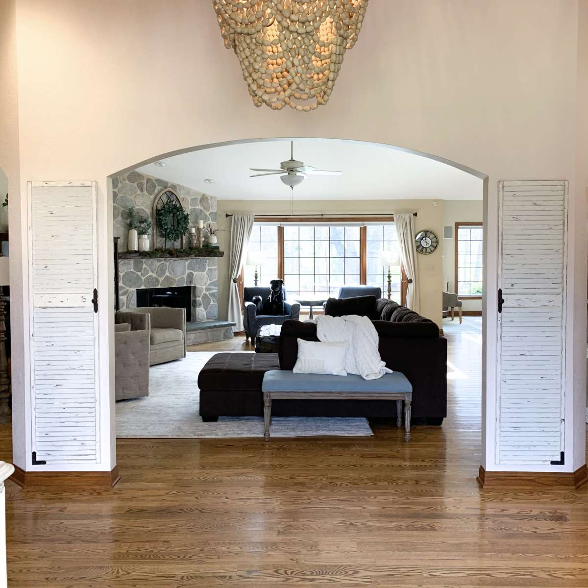 A spacious living room features a large window with natural light, a comfortable seating arrangement, and a decorative chandelier hanging from the ceiling.