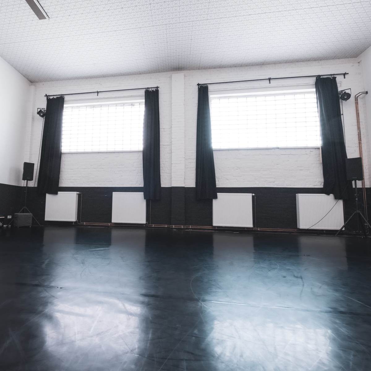 An empty dance studio with dark flooring and large windows covered by black curtains.