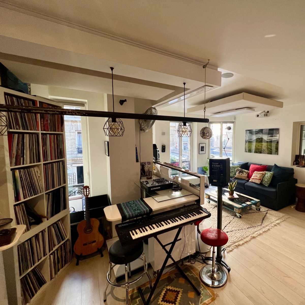 A cozy living space with a keyboard, record shelves, a guitar, and a seating area featuring a sofa and decorative items.