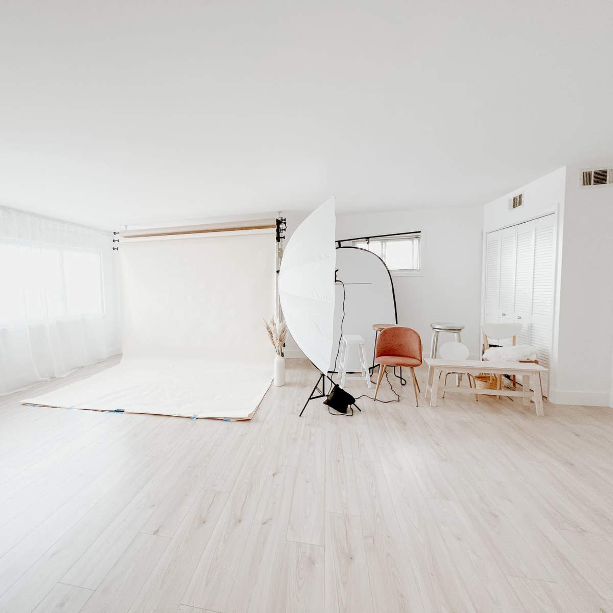A bright, spacious photo studio with a light backdrop, large windows, and various seating arrangements.