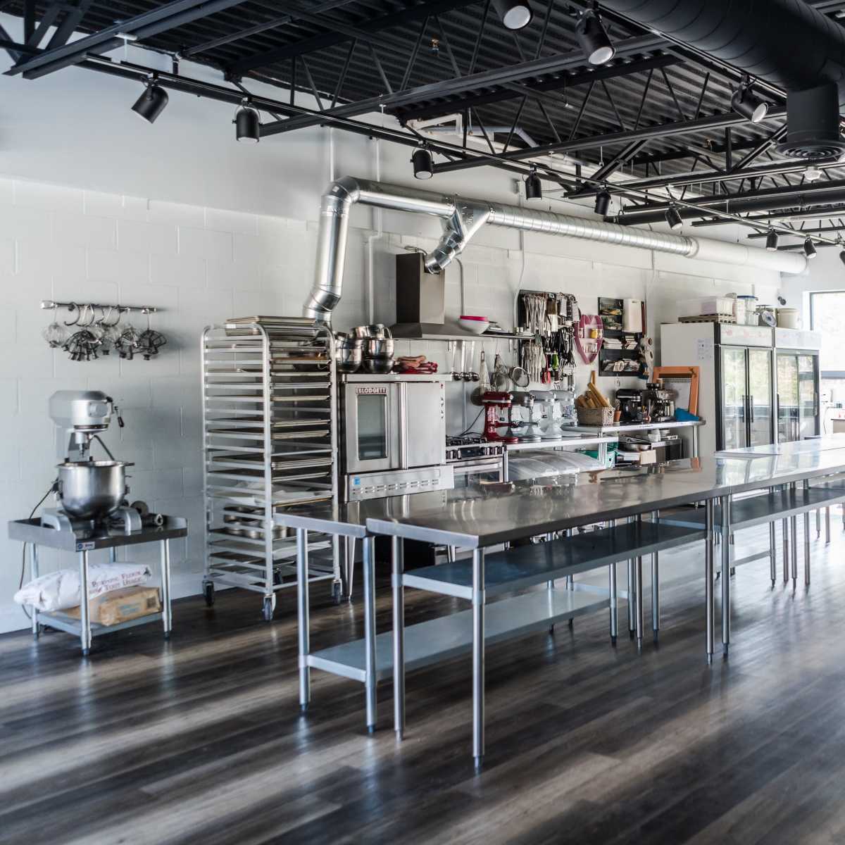 A spacious, industrial-style kitchen equipped with stainless steel tables, various appliances, and shelving units filled with kitchen supplies.