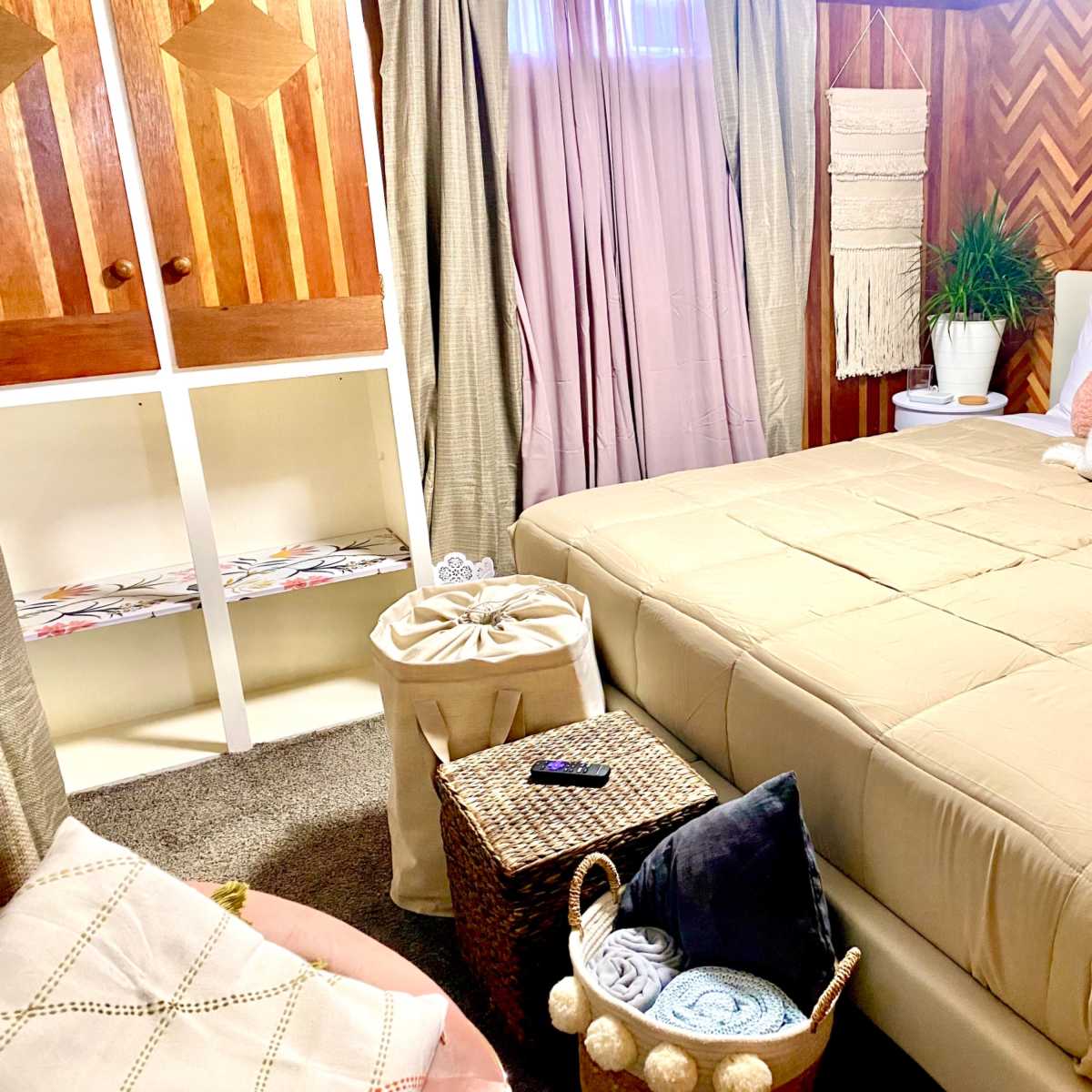 A cozy bedroom with a neatly made bed, storage baskets, and decorative elements against a patterned wood wall.
