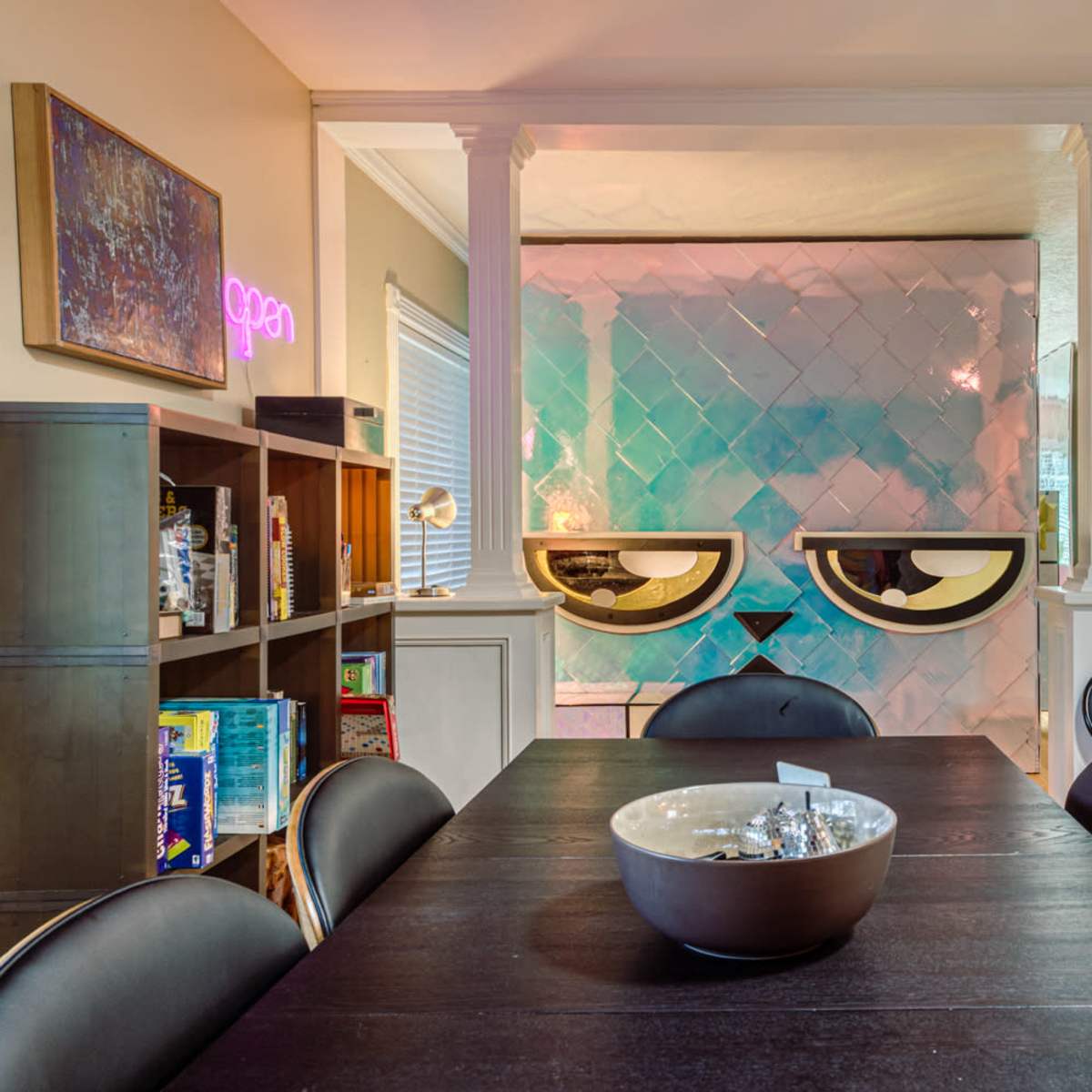 A dining area with a black table surrounded by chairs, leading to a brightly colored wall with a decorative pattern and a keyboard in the corner.