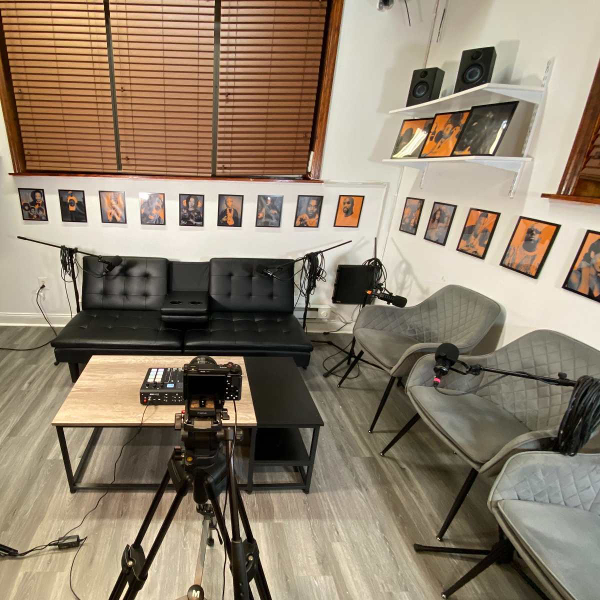 A video recording setup in a room with a black couch, two gray chairs, a wooden coffee table, and several framed pictures on the walls.