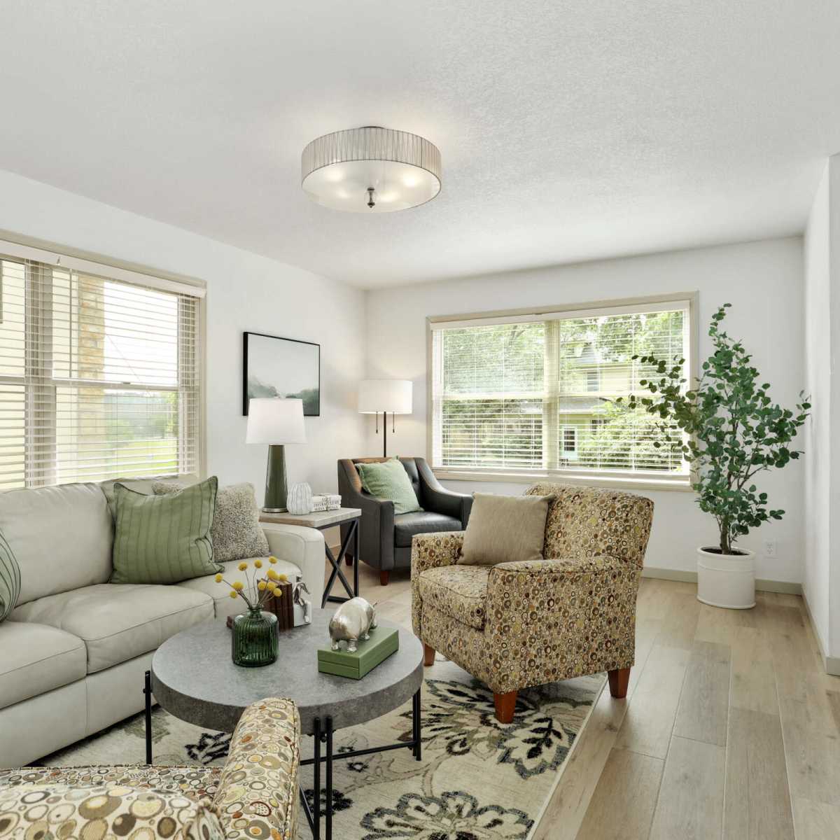 The living room features a light-colored sofa, a patterned armchair, a round coffee table, and large windows allowing natural light to fill the space.