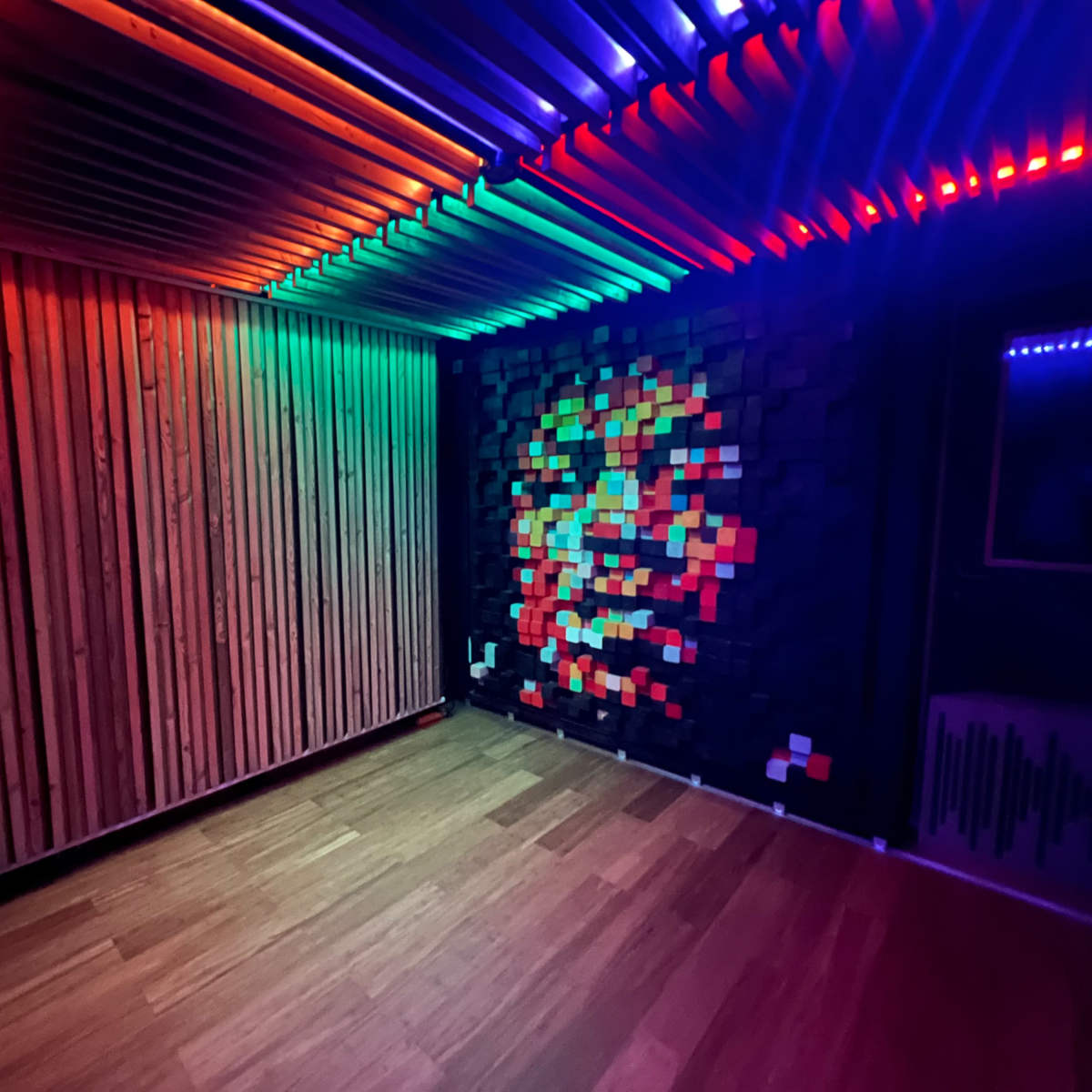 The room features wooden walls and a colorful illuminated ceiling, with a pixel art mural on one wall.
