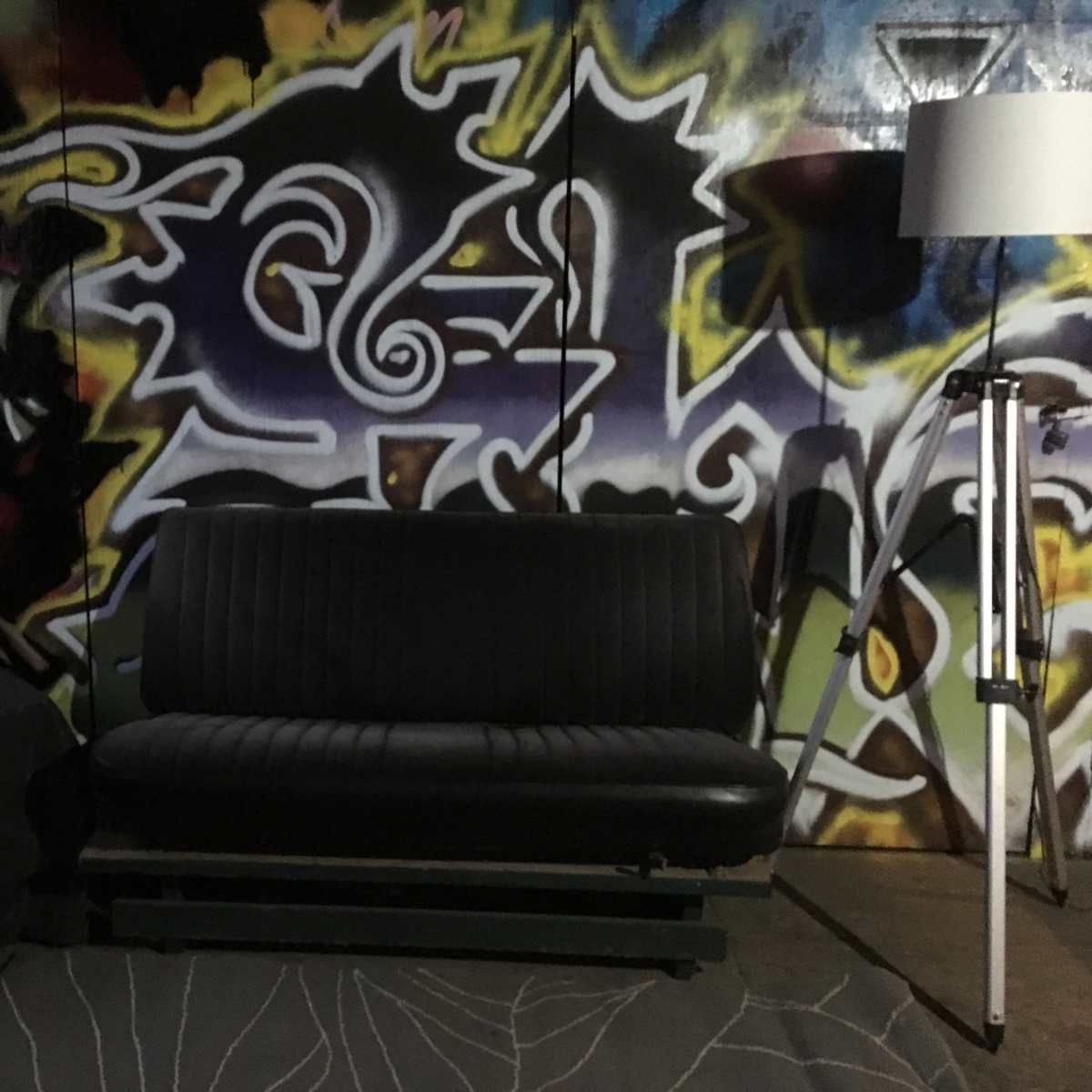 The scene features a black sofa in front of a colorful graffiti wall, accompanied by a small table and a floor lamp.
