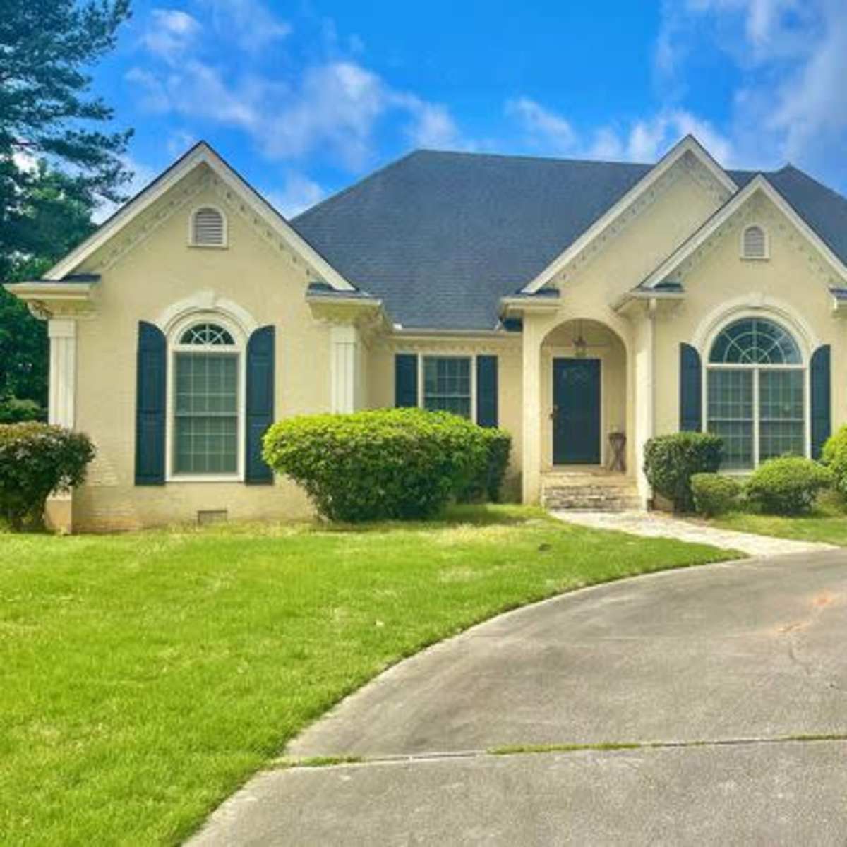 A single-story house with a spacious driveway, surrounded by well-maintained greenery and shrubs.