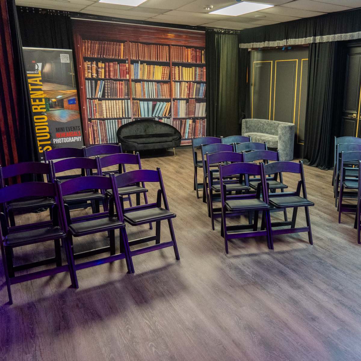 A room set up with neatly arranged black folding chairs facing a backdrop that resembles a bookshelf.