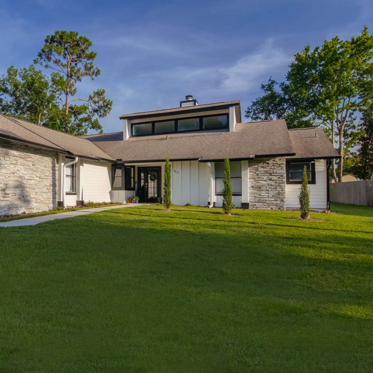 A modern house with a stone facade and spacious lawn is surrounded by trees.