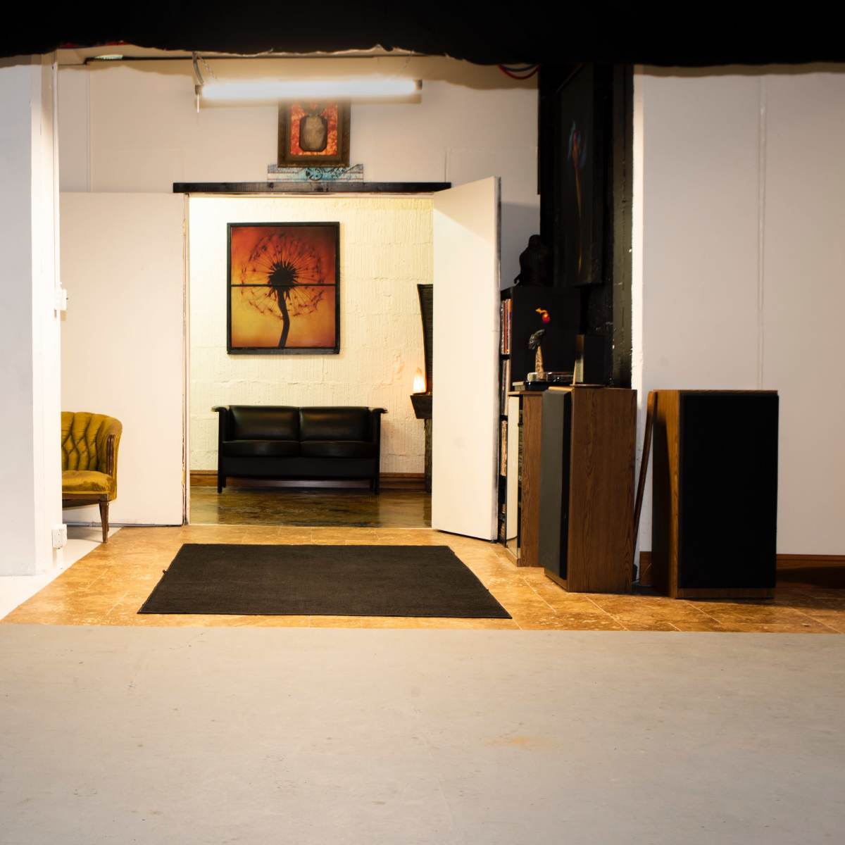 An open space leading into a room with a couch, artwork on the wall, and a mannequin near a lighting stand.