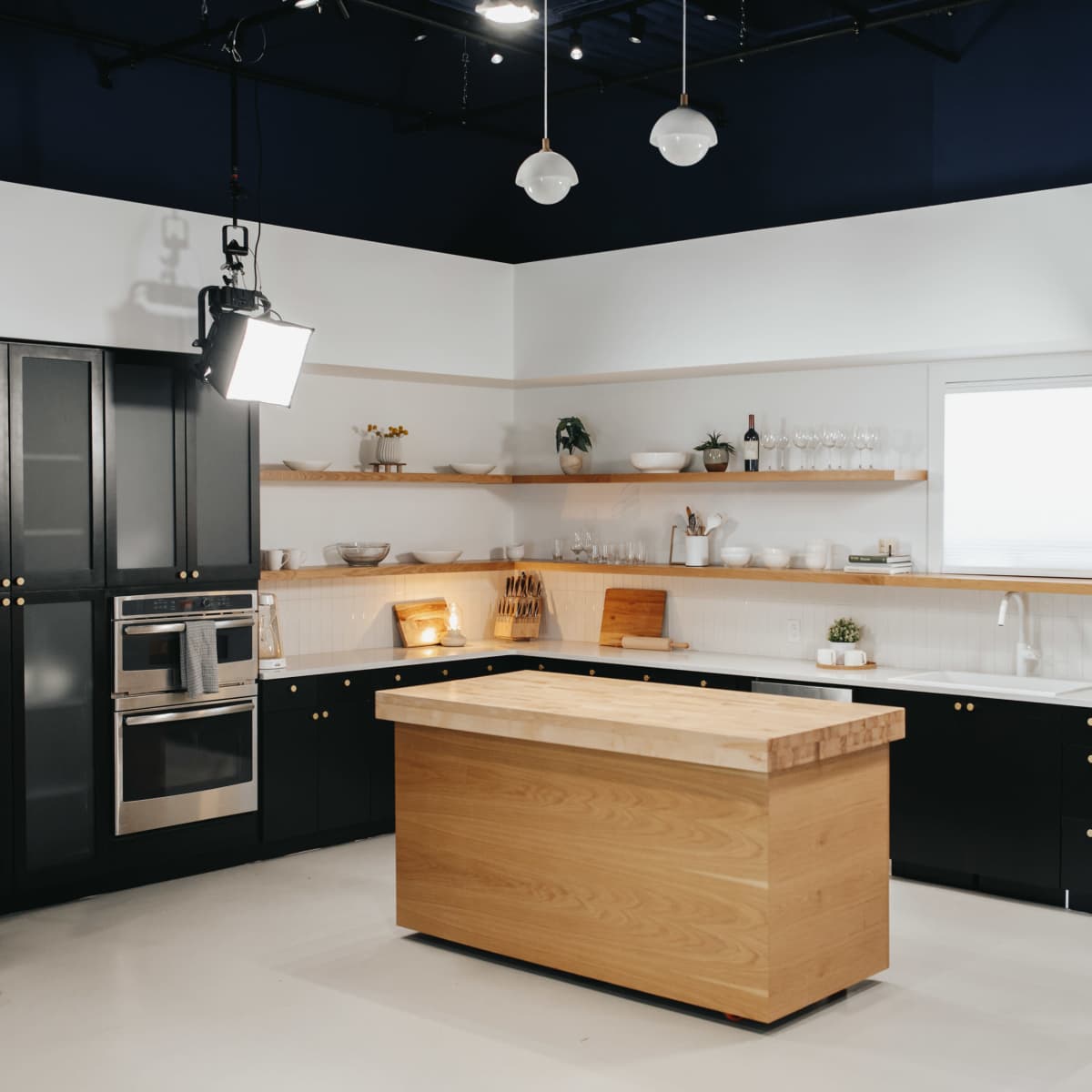 A modern kitchen with black cabinetry, a wooden island, and stainless steel appliances, featuring open shelving with kitchenware.