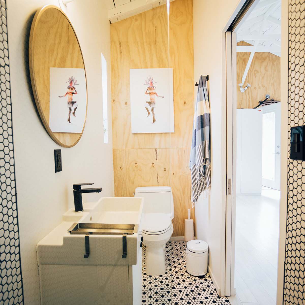 A compact bathroom features a circular mirror, a modern sink, a toilet, and a black and white hexagonal tile floor.