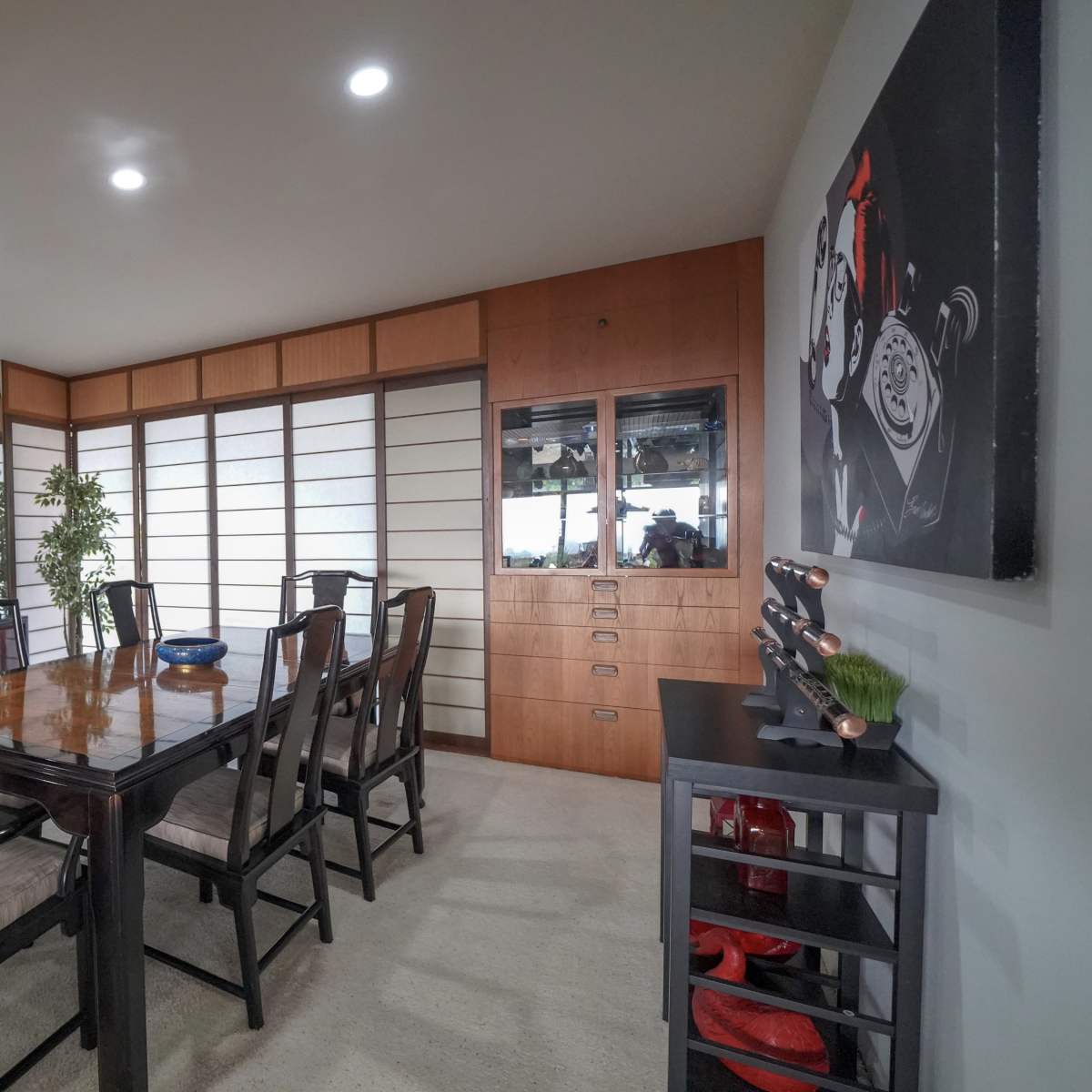 A modern dining area featuring a wooden table surrounded by black chairs, with a wall of sliding shoji-style doors and built-in storage cabinets.