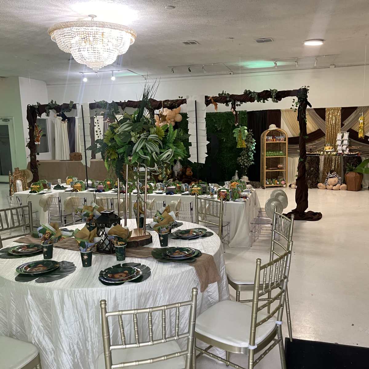 A banquet hall decorated with tables set for a celebration, featuring greenery, centerpieces, and an elaborate backdrop.