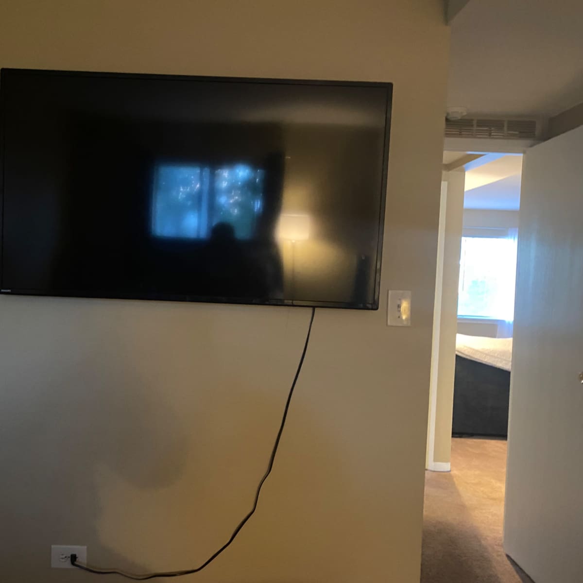 A flat-screen television is mounted on a wall with a visible power cord hanging down.