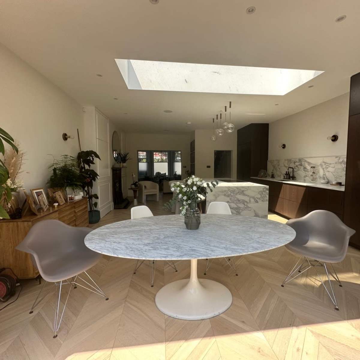 A modern dining area features a round marble table surrounded by chairs, with a skylight illuminating the space.