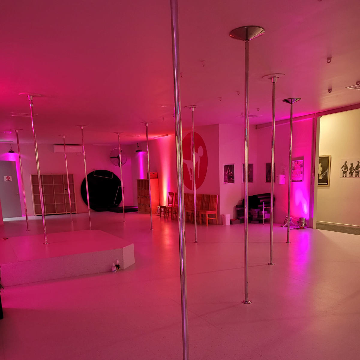 An empty dance studio with multiple metallic poles and pink ambient lighting.