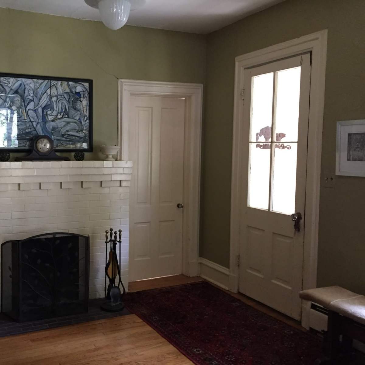 A simple entryway with a white brick fireplace, framed artwork on the wall, a wooden door, and a small area rug.