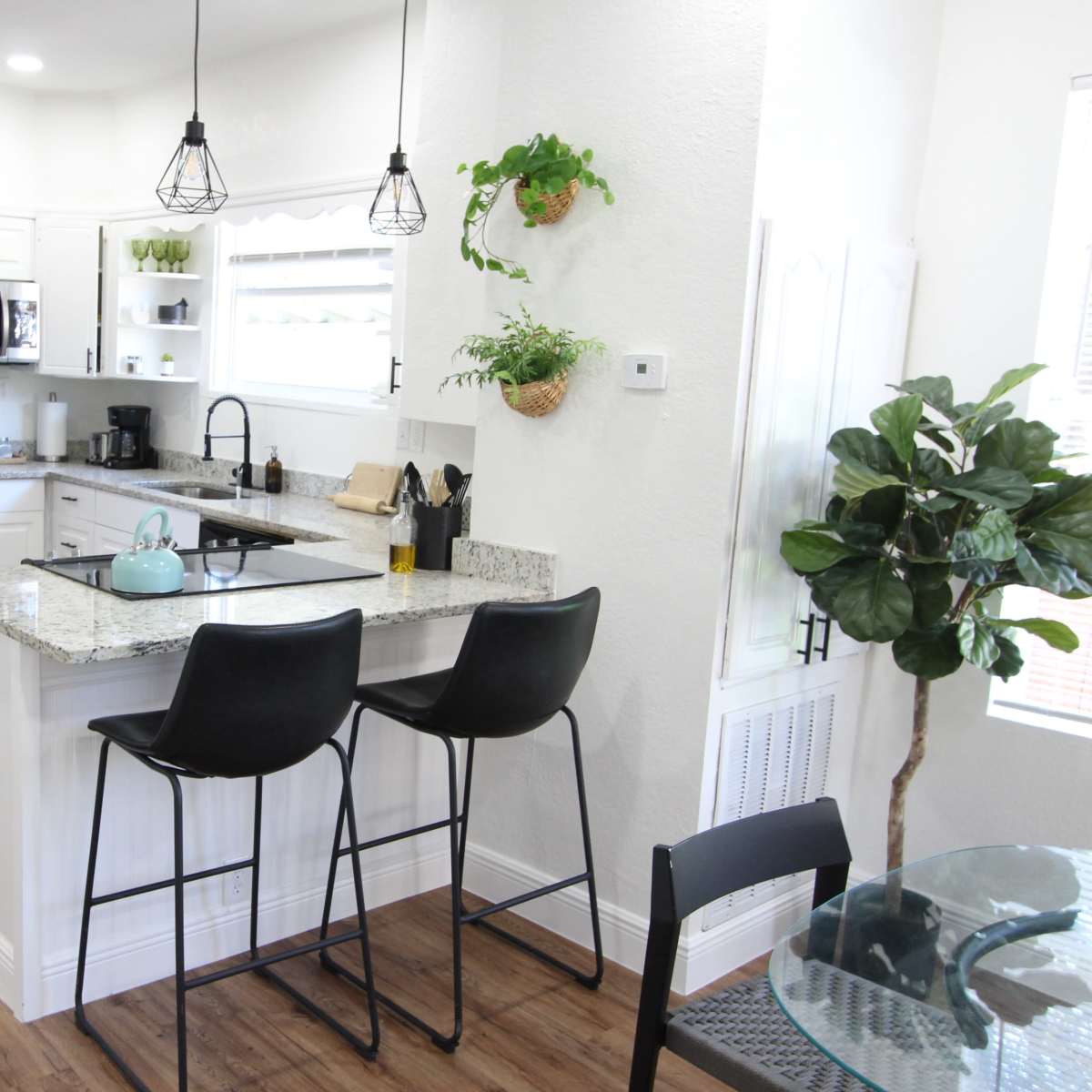 A modern kitchen features stainless steel appliances, granite countertops, and a small breakfast bar with two stools.