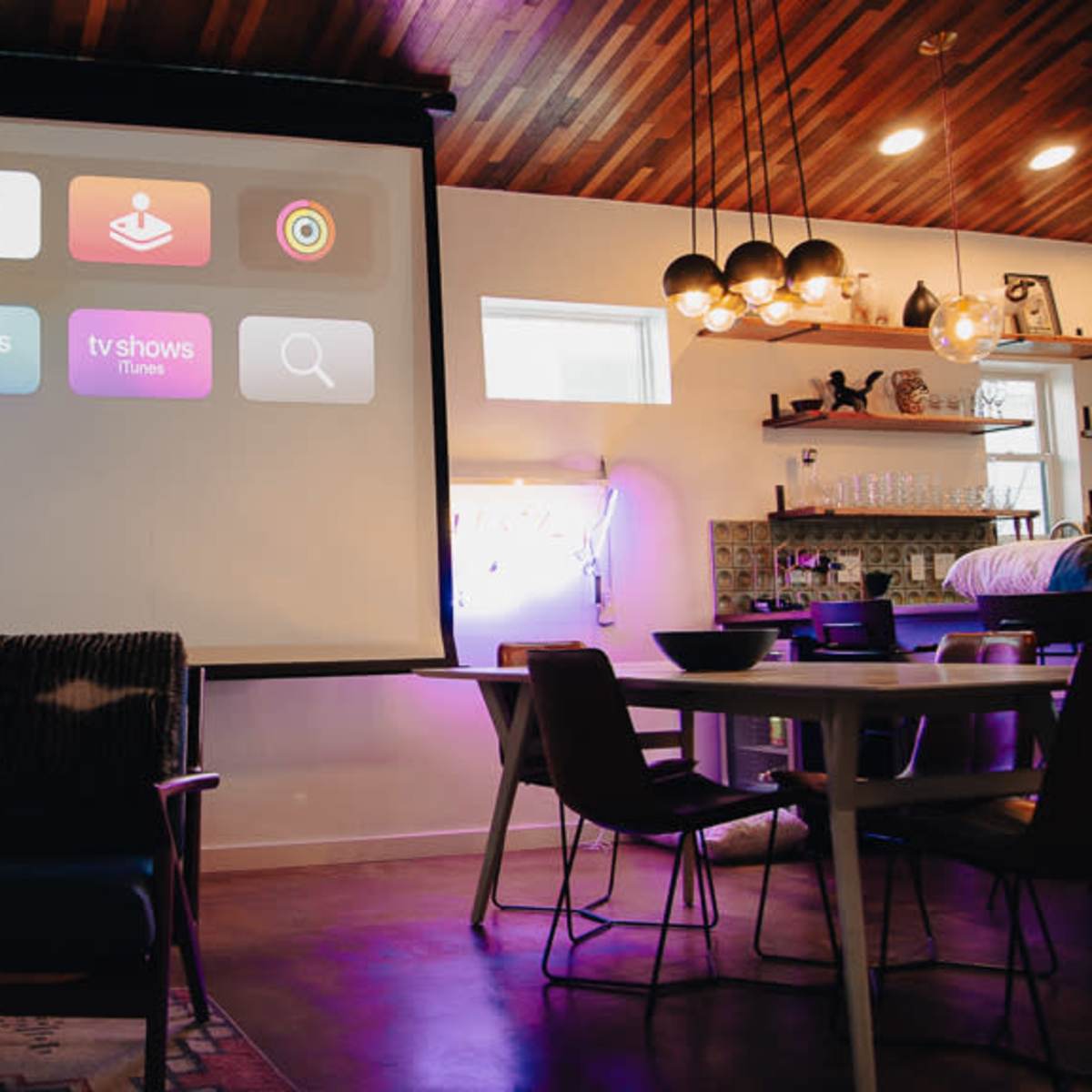 A large projection screen displays various app icons in a modern living space with stylish furniture and ambient lighting.