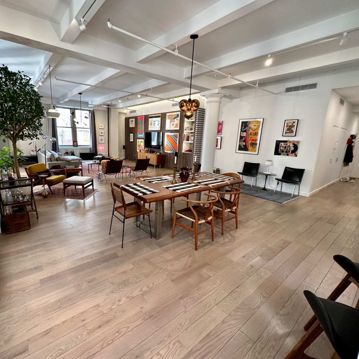 A spacious, modern dining area with a large wooden table surrounded by chairs, adorned with artwork on the walls and a mix of seating arrangements in the background.