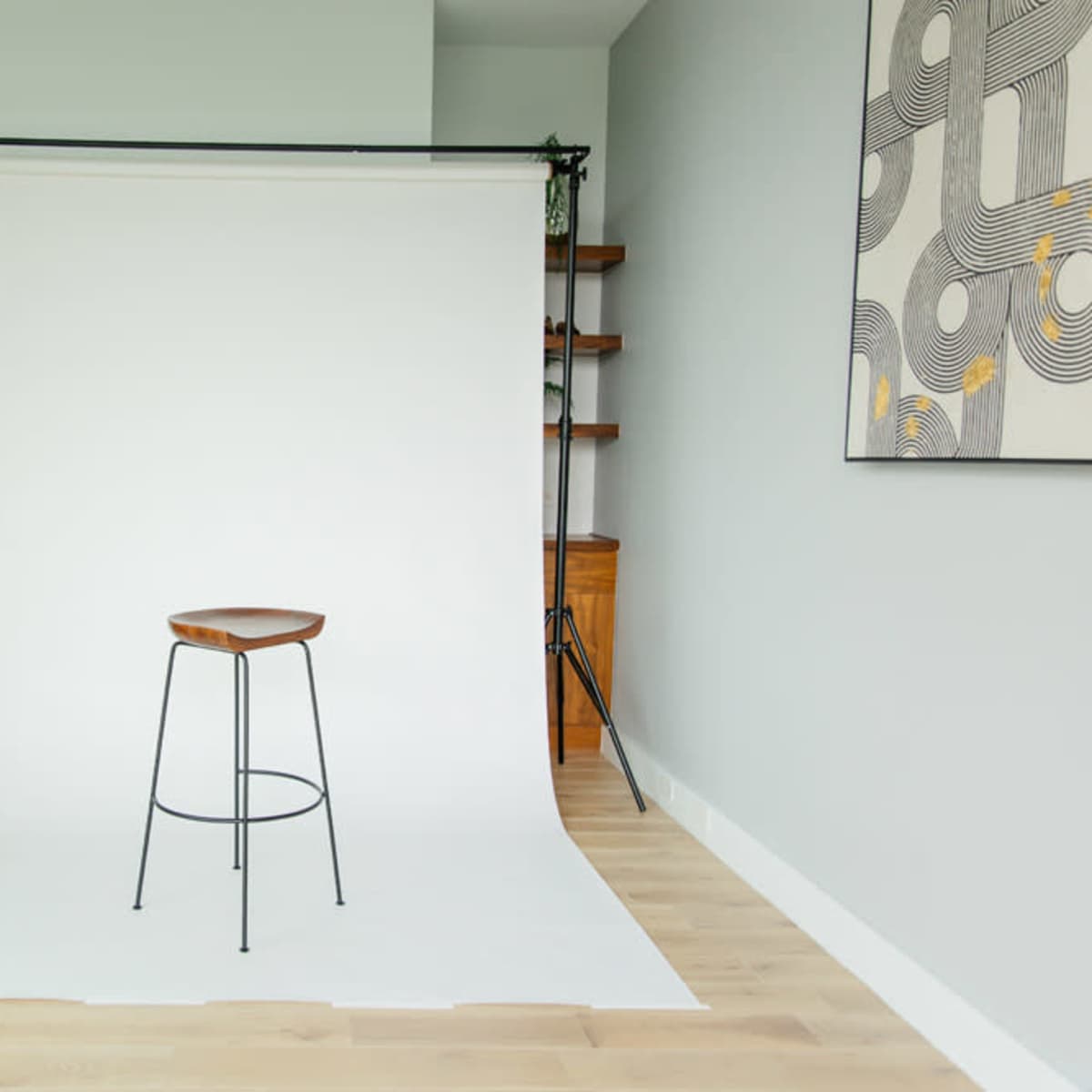 A minimalistic studio setup with a single wooden stool in front of a white backdrop and light-colored wooden flooring.