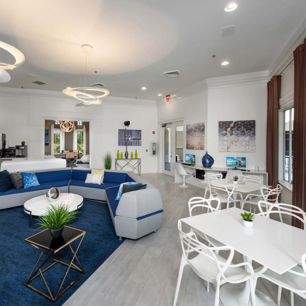 A modern lounge area featuring a blue and gray sectional sofa, circular light fixtures, and a mix of seating arrangements, including tables and chairs.