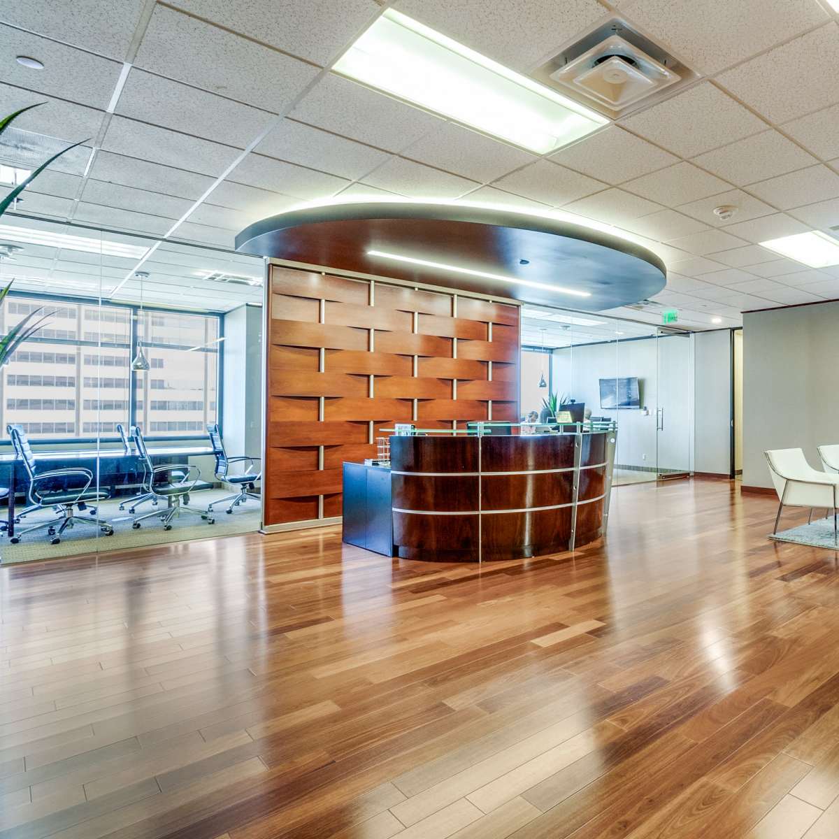 A modern office reception area with a wooden front desk, seating arrangements, and large windows overlooking a cityscape.