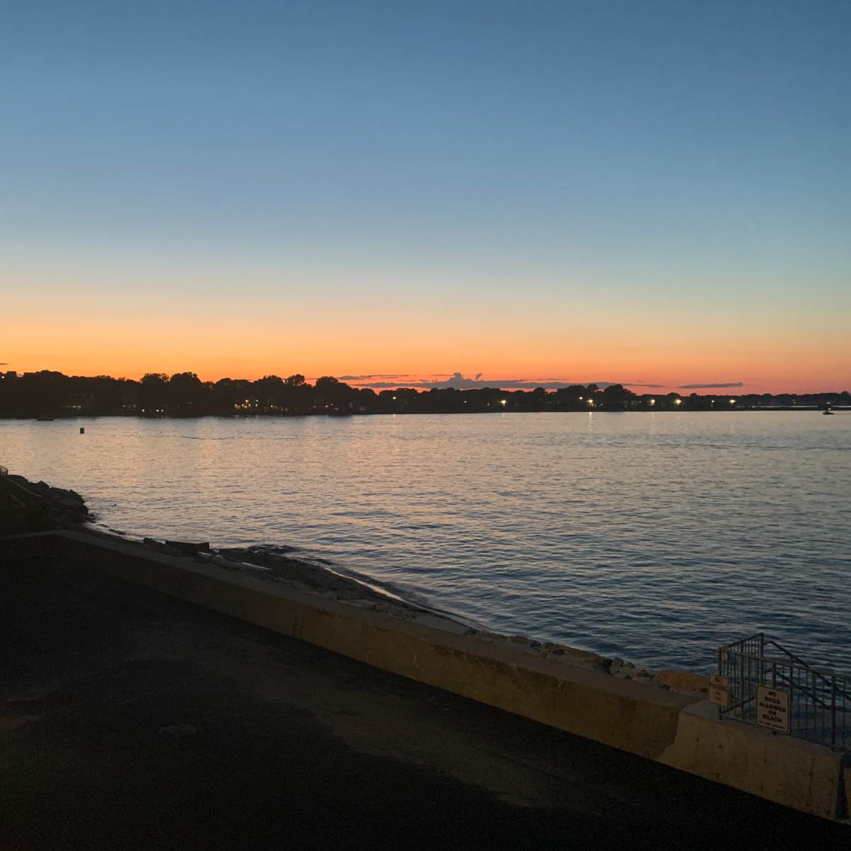 A tranquil waterfront at sunset, with orange and blue hues reflected on the water.