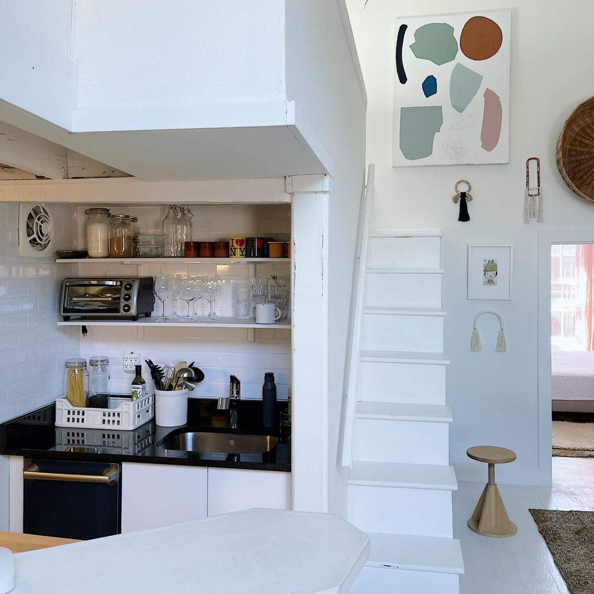 A modern kitchen with open shelving, featuring a black countertop and a staircase leading to an upper level with artwork on the wall.