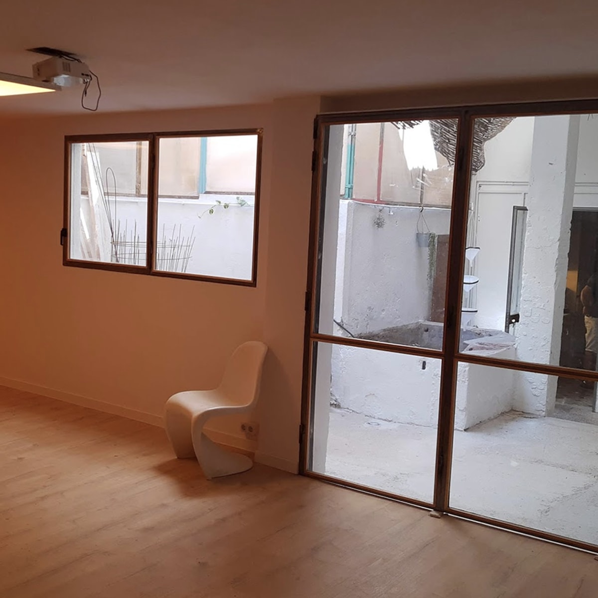 A minimalist room featuring a neon sign that reads "EL GARAGE," a white chair, and large glass doors leading to an outdoor area.