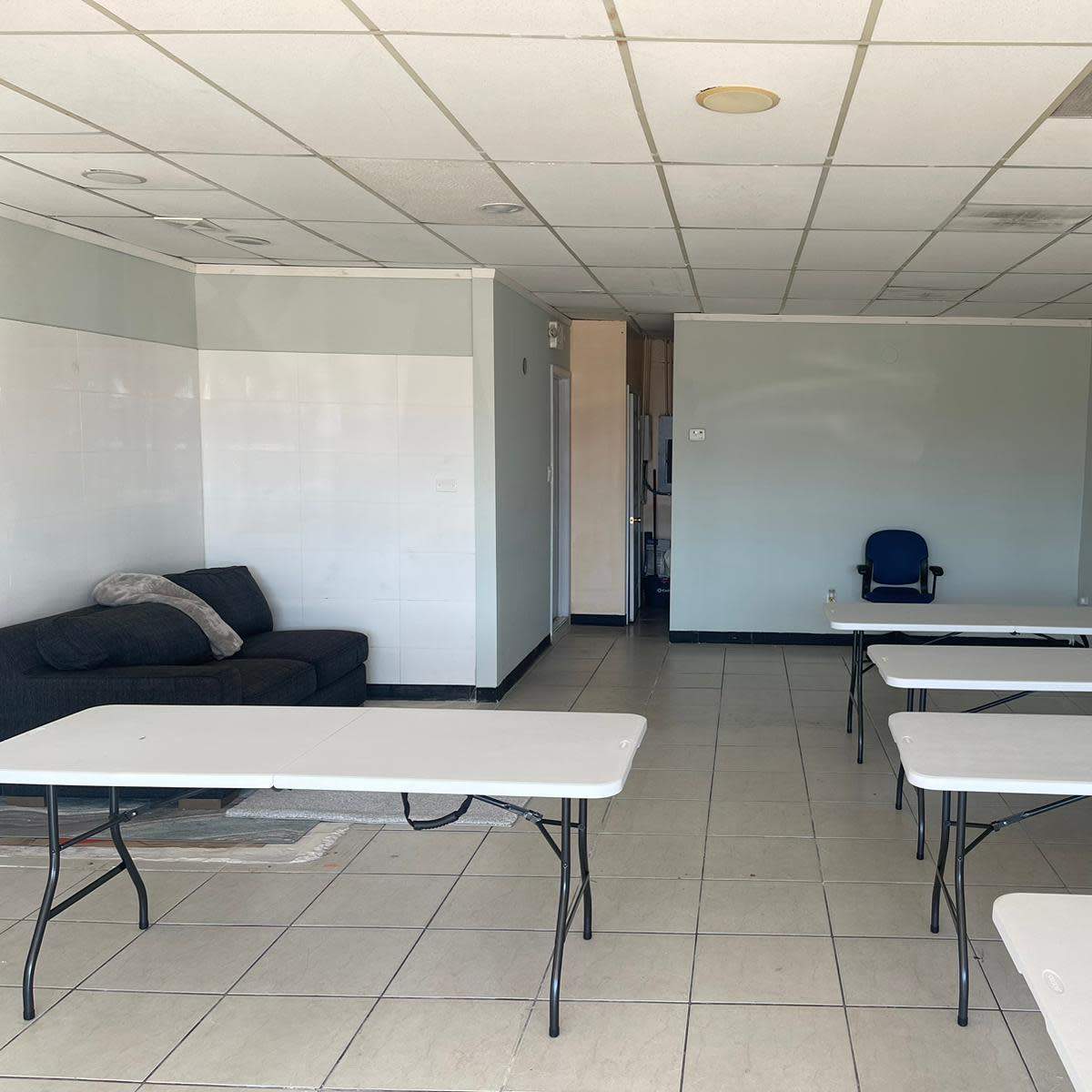A sparsely furnished room with a couch on one side and several folding tables arranged throughout the space.